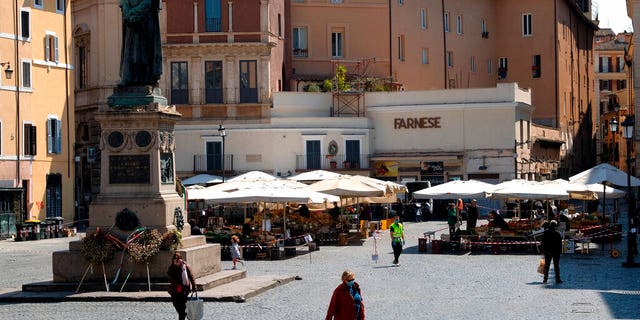 People shopping at Campo de Fiori fresh fruits and vegetables open market, as the statue of Giordano Bruno watches over the square, in Rome, Tuesday, April 7, 2020. 