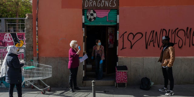 Volunteers, wearing face masks and gloves, distribute food bags at the "Dragones de Lavapies" soccer association in Madrid, Spain, Wednesday. Amid the coronavirus lockdown, volunteers meet at the soccer youth club to distribute food to hundreds of families at risk of social exclusion. (AP Photo/Bernat Armangue)