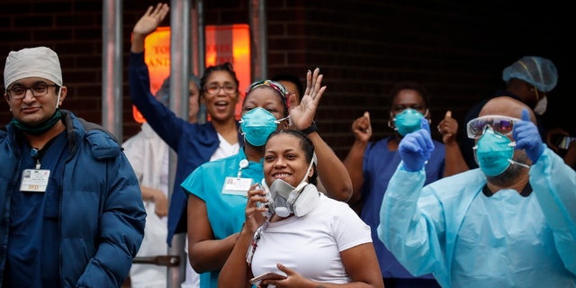 Medical workers cheer and acknowledge pedestrians and FDNY firefighters who gathered to applaud them at 7 p.m. outside Brooklyn Hospital Center on Tuesday in New York.  (AP Photo/John Minchillo)