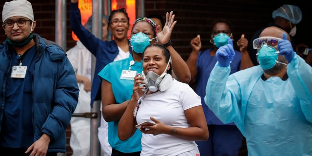 Medical workers cheer and acknowledge pedestrians and FDNY firefighters who gathered to applaud them at 7 p.m. outside Brooklyn Hospital Center on Tuesday in New York.  (AP Photo/John Minchillo)