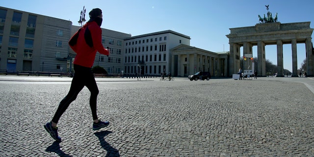 In this March 24, 2020, file photo, a man jogs on the square in front of the Brandenburg Gate in Berlin, Germany. As the restrictions are eased, Chancellor Angela Merkel has pointed to South Korea as an example of how Germany will have to improve measures to “get ahead” of the pandemic with more testing and tracking of cases so that the rate of infections can be slowed.