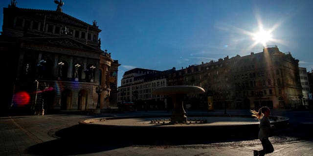 A woman running along the Old Opera, left, in Frankfurt, Germany, early Sunday. Germany has maintained its coronavirus restrictions but announced planned changes.