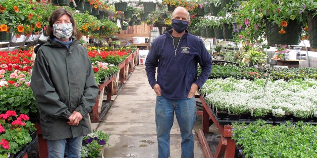 In this Monday April 27, 2020, photo, owners Carol and Mike MacLeod pose in one of the greenhouses of Evergreen Gardens of Vermont in Waterbury Center, Vt. Monday was the first day businesses such as greenhouses and garden centers could allow a small number of customers inside as part of Vermont's gradual coronavirus pandemic reopening plan. (AP Photo/Wilson Ring)