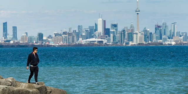 A man walks on rocks by Lake Ontario with the downtown core in the backdrop in Toronto, Monday, April 27, 2020.
