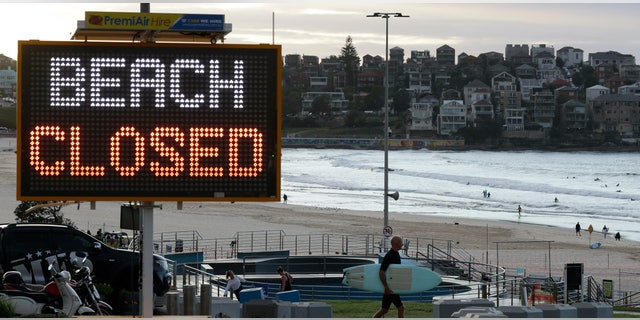 A sign indicates the beach is closed as a surfers arrives for the 7A.M. opening of Bondi Beach in Sydney, Tuesday, April 28, 2020, as coranavirus pandemic restrictions are eased. The beach is open to swimmers and surfers to exercise only.