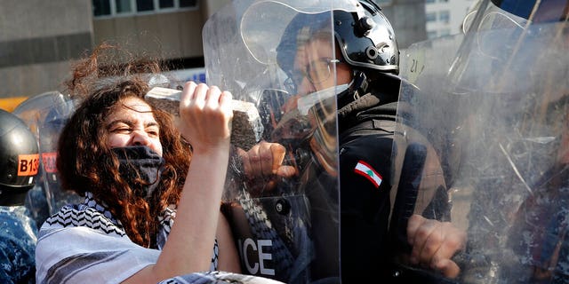 An anti-government protester uses stone to beat on the shield of a riot policeman, during a protest against the deepening financial crisis, in Beirut, Lebanon, Tuesday, April 28, 2020.