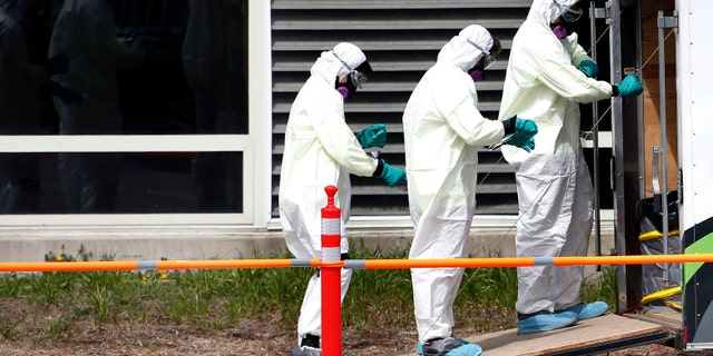 In this March 31, 2020 photo, cleaners unwrap their protective gear as they leave the Soldiers' Home in Holyoke, Mass. Nearly 70 residents have died from the coronavirus at the central Massachusetts home for aging veterans. (Jessica Rinaldi/The Boston Globe via AP, File)