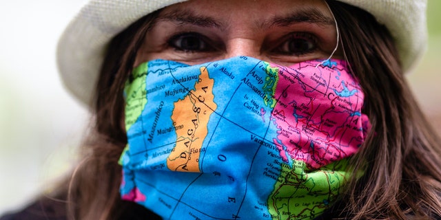 A woman wears a face mask with a world map design as the attends a protest of travel agents in Kiel, Germany, Wednesday, Aril 29, 2020. Representatives of tour operators and travel agencies demonstrated in front of the Kiel state parliament to draw attention to their difficult economic situation during the coronavirus crisis.
