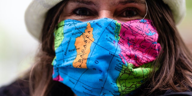 A woman wears a face mask with a world map design as the attends a protest of travel agents in Kiel, Germany, Wednesday, Aril 29, 2020. Representatives of tour operators and travel agencies demonstrated in front of the Kiel state parliament to draw attention to their difficult economic situation during the coronavirus crisis.