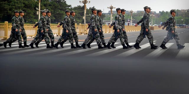Chinese military personnel walk across a street adjacent to Tiananmen Square in Beijing, Wednesday, April 29, 2020.