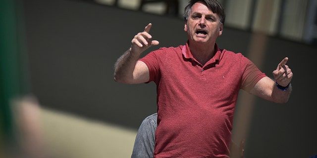 Brazil's President Jair Bolsonaro speaks to supporters during a protest asking for military intervention in front the army's headquarters during the new coronavirus pandemic, in Brasilia, Brazil, Sunday, April 19, 2020. Bolsonaro came out in support of a small protest Sunday that defended military intervention, infringing his own ministry's recommendations to maintain social distancing and prompting fierce critics. (AP Photo/Andre Borges)