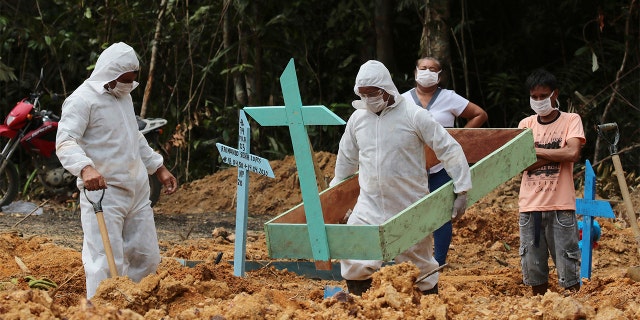 In this April 16, 2020 photo, funeral workers in protective gear prepare the grave of a woman who is suspected to have died of COVID-19 disease, at the Nossa Senhora Aparecida cemetery, in Manaus, Amazonas state, Brazil. Gravediggers buried 60 people that day, about triple the pre-virus average, according to a cemetery official. (AP Photo/Edmar Barros)