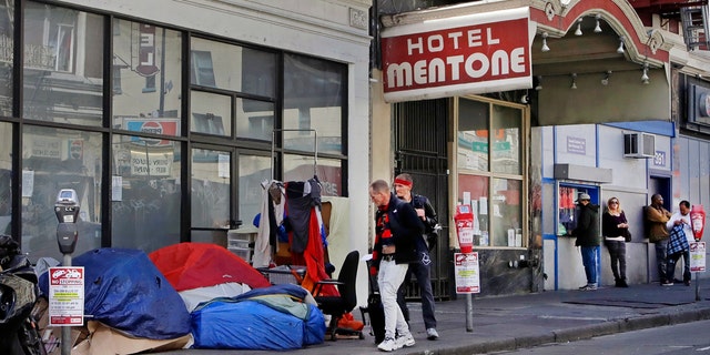 In this Monday, April 13, 2020, file photo, pedestrians walk to the edge of the sidewalk to avoid stepping on people in tents and sleeping bags in the Tenderloin area of San Francisco.