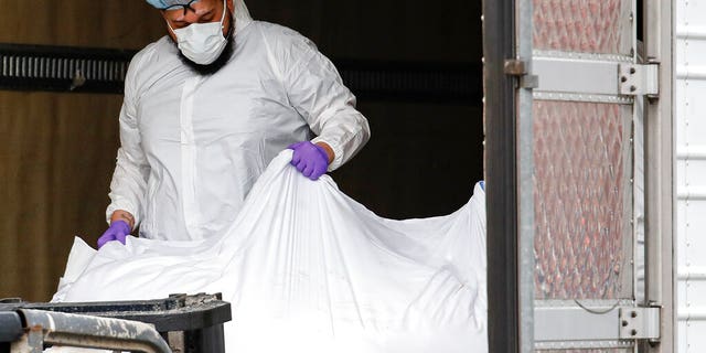 A body wrapped in plastic is loaded onto a refrigerated container truck used as a temporary morgue by medical workers wearing personal protective equipment due to COVID-19 concerns, Tuesday, March 31, 2020, at Brooklyn Hospital Center in the Brooklyn borough of New York. (AP Photo/John Minchillo)