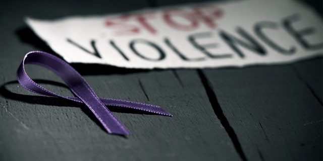 A purple ribbon lays next to a sign bringing awareness to domestic violence.