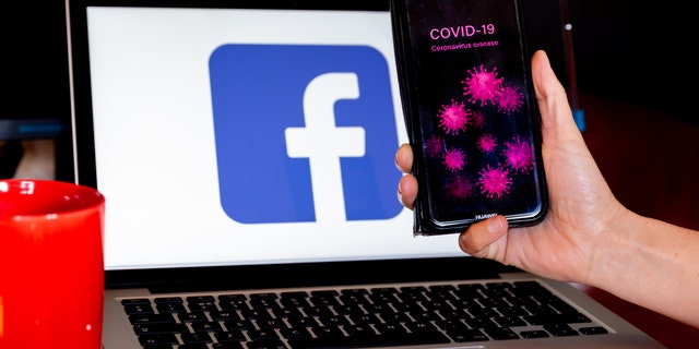 A woman holds her mobile phone in front of a computer screen with facebook logo for illustration purposes during Coronavirus pandemic, Ostrowiec Swietokrzyski on April 14, 2020.