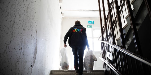 Pastor Bernd Siggelkow founder of the Christian charity the Arche, or Ark, carries bags with donated goods for poor families up the stairs of a center of the organization in Berlin, Germany, Tuesday, March 31, 2020. (AP Photo/Markus Schreiber)