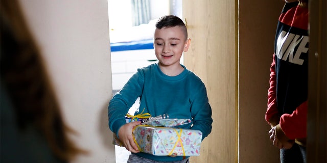 Sali, center, receives a birthday present from social worker Rebekka Rauchhaus of the Christian charity the Arche, or Ark, while his mother Janet, right, stands beside him at the doorsteps of their apartment in the Hellersdorf suburb of Berlin, Germany, Thursday. (AP Photo/Markus Schreiber)