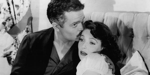 Orson Welles kissing Loretta Young sitting in bed in a scene from the film 'The Stranger,' 1946.