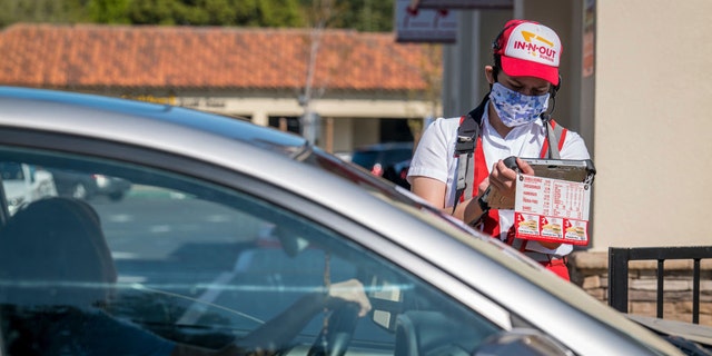 A worker at an In-N-Out restaurant in California is seen wearing a cloth face covering as he takes an order from a customer waiting in a drive-thru line on Tuesday, April 7, 2020.