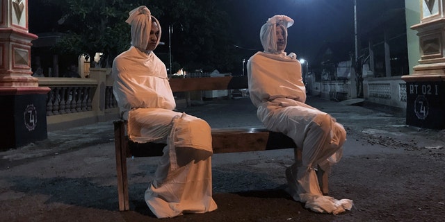 Volunteers Deri Setyawan, 25, and Septian Febriyanto, 26, sit on a bench as they play the role of 'pocong', or known as 'shroud ghost', to make people stay at home amid the spread of coronavirus in one village in Indonesia.