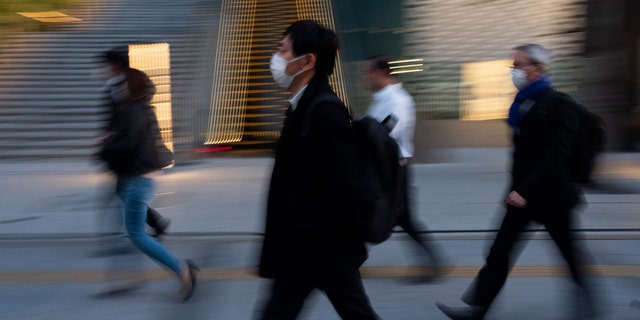 Commuters walk along a sidewalk Monday, April 6, 2020, in Tokyo.