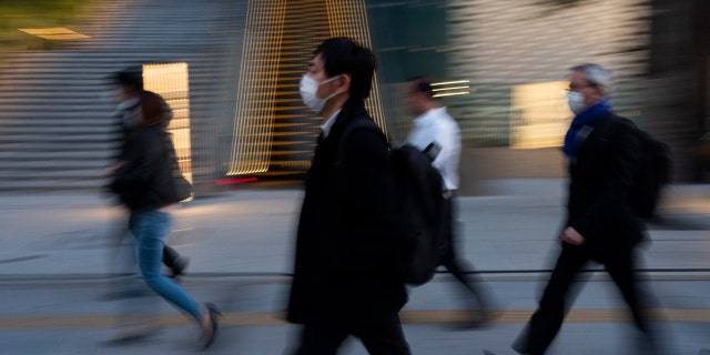 Commuters walk along a sidewalk Monday, April 6, 2020, in Tokyo.