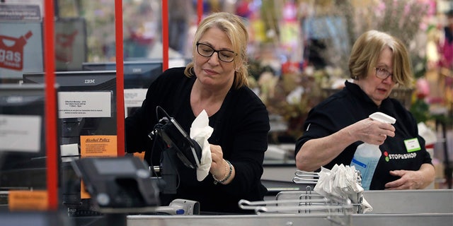 Cashiers at a grocery store sanitize a card reader and the checkout area, March 26, in Quincy, Mass., as an extra precaution out of concern about the spread of the coronavirus. (AP Photo/Steven Senne)