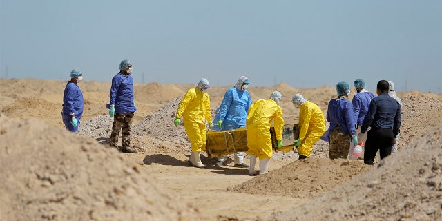 FILE - In this March 30 photo, Iraqi health ministry workers carry a coffin of a person who died from coronavirus at a new cemetery for the people who died from Covid-19 outside the town of Najaf, Iraq. Across the Middle East and parts of South Asia, bereaved families have faced traumatic restrictions on burying their dead amid the pandemic. Religion and customs that require speedy burials in the largely Muslim region have clashed with fears of COVID-19 contagion and government-mandated lockdowns. (AP Photo/Anmar Khalil, File)