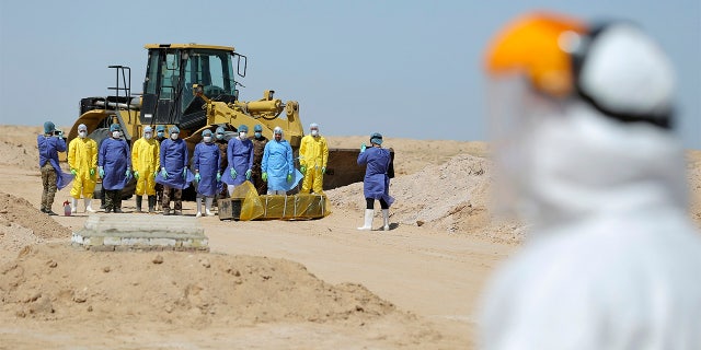 File - In this March 30 photo, Iraqi health ministry workers pray by a coffin of a person who died from coronavirus at a new cemetery for the people who died from Covid-19 outside the town of Najaf, Iraq. Across the Middle East and parts of South Asia, bereaved families have faced traumatic restrictions on burying their dead amid the pandemic. Religion and customs that require speedy burials in the largely Muslim region have clashed with fears of COVID-19 contagion and government-mandated lockdowns. (AP Photo/Anmar Khalil, File)