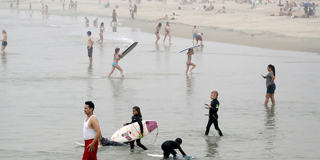 Swimmers and surfers wade in the water Sunday, April 26, 2020, in Newport Beach, Calif. A lingering heat wave lured people to California beaches, rivers and trails again Sunday, prompting warnings from officials that defiance of stay-at-home orders could reverse progress and bring the coronavirus surging back.