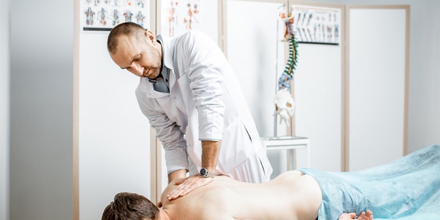 Fisioterapeuta senior profesional que realiza un tratamiento manual en la columna torácica de un hombre.