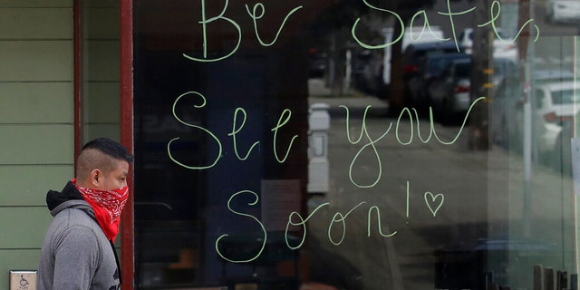 A man wears a bandana on his face as he walks past a sign written on the window of a Starbucks coffee shop, which was closed for coronavirus concerns, in San Francisco, Tuesday, March 24, 2020.