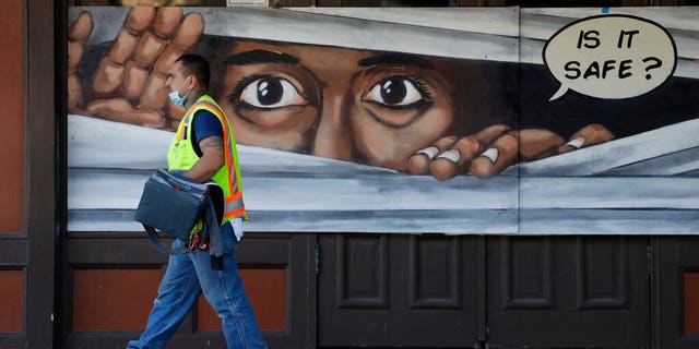 A construction worker walks past a mural painted on a boarded up business that is temporarily closed due to the COVID-19 pandemic, in Austin, Texas. Texas Gov. Greg Abbott announced he is relaxing some restrictions that have been imposed on some businesses. (AP Photo/Eric Gay)