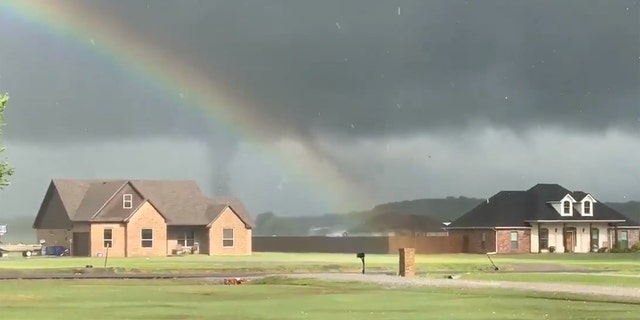 A tornado forms and passes behind houses at Lake Durant in Oklahoma as a rainbow is visible in the foreground on April 22, 2020.