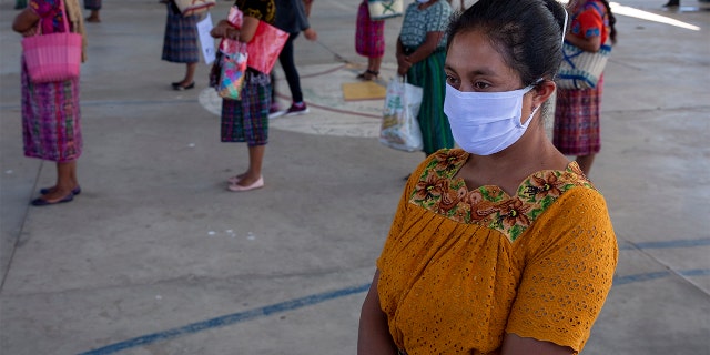 In this April 3, 2020 photo, women wearing protective face masks stand at a safe distance to help curb the spread of the new coronavirus, as they wait for food assigned to their children outside a school in the largely indigenous Xesuj village, Guatemala, where many residents depend on remittances, almost all from the U.S. The devastation wrought by COVID-19 across the developed world is cutting into the financial lifelines for people across Latin America, Africa and Asia. 