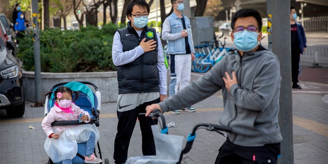 People stand along a street during a national moment of mourning for victims of the coronavirus, in Beijing, on Saturday. (AP)
