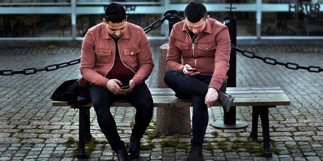 In this Wednesday, April 8, 2020 file photo two men check their phones as they sit near the harbor in Stockholm, Sweden. (AP Photo/Andres Kudacki, File)
