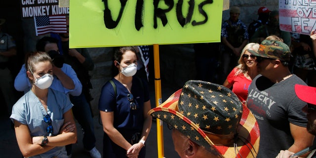 Caregivers stand in front of protesters at the main entrance to the Arizona Capitol at a rally to 're-open' Arizona against the governor's stay-at-home order due to the coronavirus Monday, April 20, 2020, in Phoenix. (AP Photo/Ross D. Franklin)