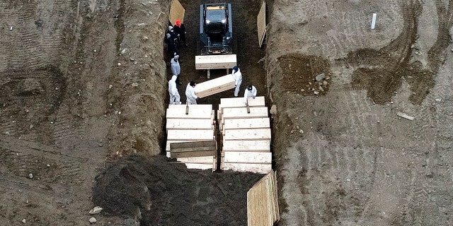 Workers wearing personal protective equipment bury bodies in a trench on Hart Island in New York City's Bronx borough on Thursday. (AP)