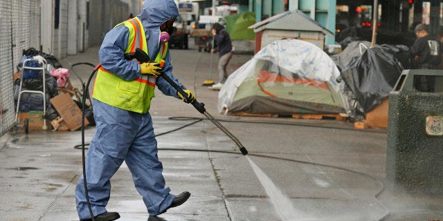 In this Feb. 26, 2016, file photo, a city worker uses a power washer to clean the sidewalk by a tent city along Division Street in San Francisco.