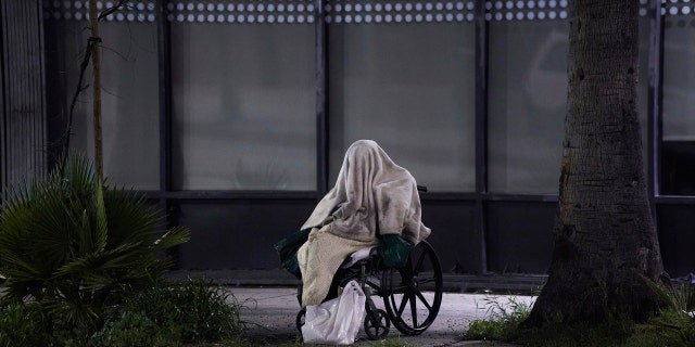 In this April 6, 2020, file photo, a homeless person sits on a wheelchair in rainy weather on Sunset Boulevard in Los Angeles.