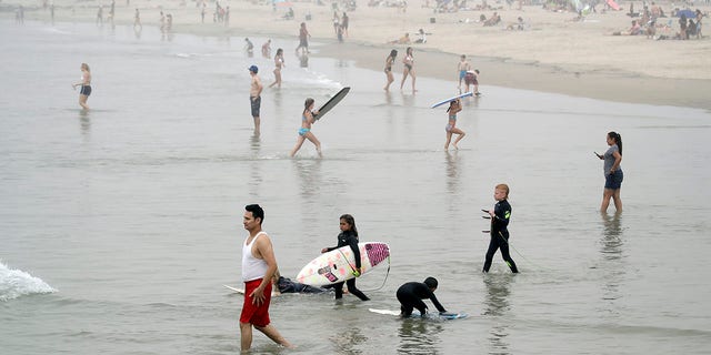 Swimmers and surfers wade in the water Sunday, April 26, 2020, in Newport Beach, Calif. A lingering heat wave lured people to California beaches, rivers and trails again Sunday, prompting warnings from officials that defiance of stay-at-home orders could reverse progress and bring the coronavirus surging back. (AP Photo/Marcio Jose Sanchez)