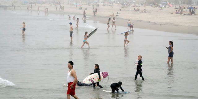 Swimmers and surfers wade in the water Sunday, April 26, 2020, in Newport Beach, Calif. A lingering heat wave lured people to California beaches, rivers and trails again Sunday, prompting warnings from officials that defiance of stay-at-home orders could reverse progress and bring the coronavirus surging back. (AP Photo/Marcio Jose Sanchez)