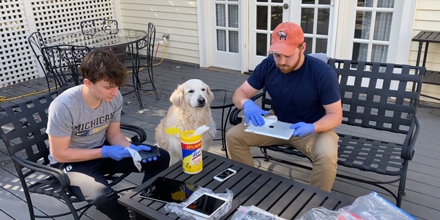 Sam and Ben Hitt sanitize donated iPads outside their house, with dog Abby observing.