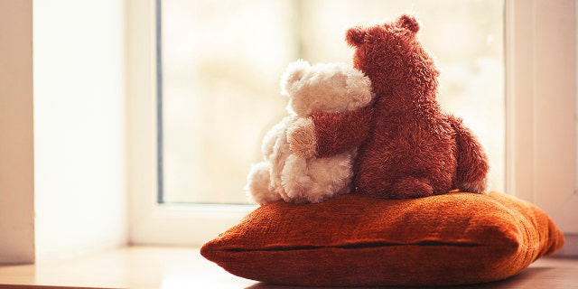 Two embracing teddy bears looking through the window sitting on window-sill.