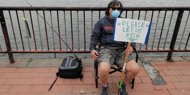 Ray Kawabata holds a sign that reads "Please Let Us Fish" at Gas Works Park in Seattle on April 26, during a protest against Washington state's current ban on fishing due to stay-at-home orders implemented to prevent the spread of the coronavirus. (AP Photo/Ted S. Warren)