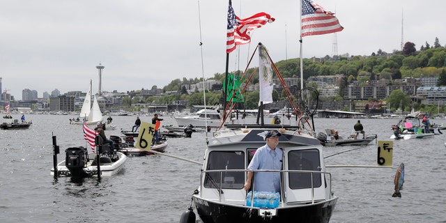 A protester reels in a fake fish near poles marking a six-foot social distance on a boat on Lake Union near Gas Works Park in Seattle on April 26. (AP Photo/Ted S. Warren)