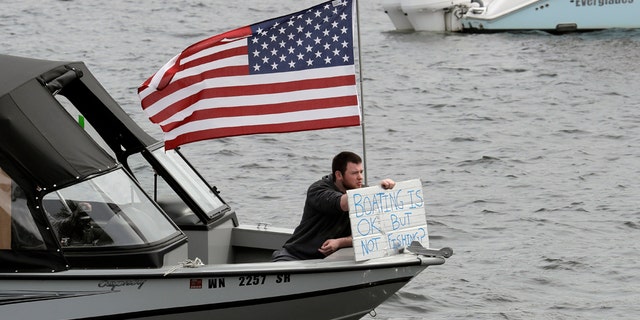 A protester hold a sign that reads "Boating is OK, but Not Fishing?" as he sits on a boat on Lake Union near Gas Works Park in Seattle on April 26. (AP Photo/Ted S. Warren)