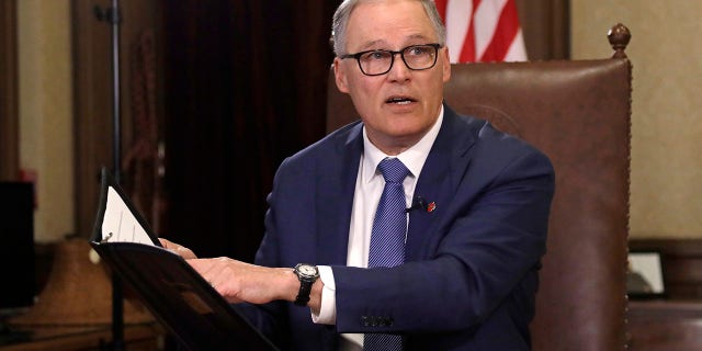 Gov. Jay Inslee turns to staff members as he prepares to speak about additional plans to slow the spread of coronavirus before a televised address from his office on March 23 in Olympia, Wash. (AP Photo/Elaine Thompson)